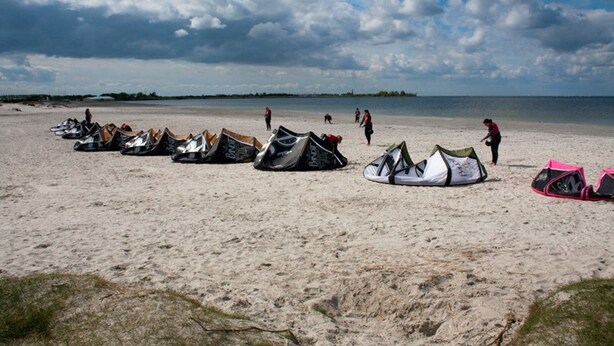 Una playa con varias tiendas de campaña montadas, algunas personas caminando y una masa de agua al fondo.