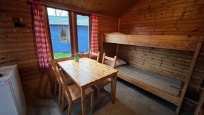 Una cabaña con literas, una mesa de madera con sillas y un ventanal con cortinas.