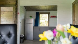Et lille køkken med køleskab, vask og et vindue med blå gardiner.