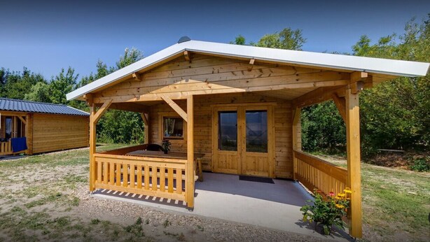 A wooden cabin with a porch, a small deck, and a covered outdoor seating area.