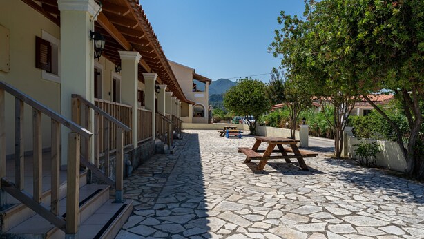 A courtyard with stone flooring, wooden benches, and a staircase leading to a building with a tiled roof. - Apartment 'Deluxe Quadruple Room 1' with Mountain View, Wi-Fi and Air Conditioning (Acharavi)