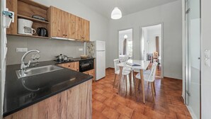 Una cucina con un piano di lavoro nero, mobili in legno, un frigorifero bianco e un'area pranzo con tavolo e sedie bianche.