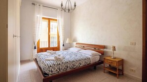Ein Schlafzimmer mit einem hölzernen Bett, einem Nachttisch, einer Lampe und Blick auf den Balkon.