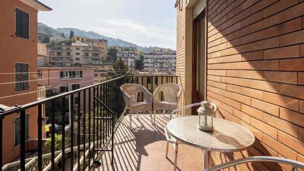 Ein Balkon mit Korbstühlen und einem kleinen Tisch, mit Blick auf eine Stadtlandschaft aus Gebäuden und Hügeln.