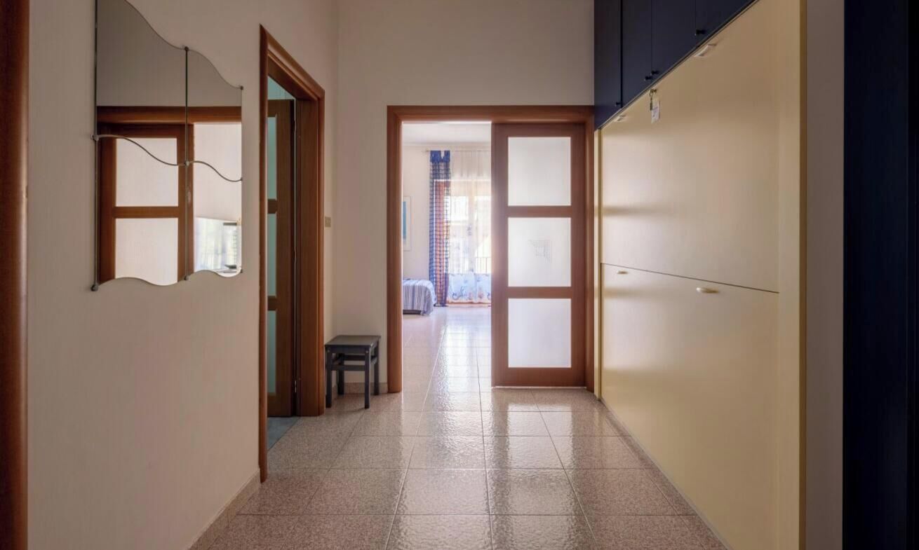 Un couloir avec un sol carrelé, des portes en bois et un petit tabouret.