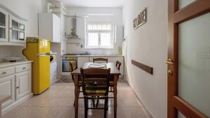 Eine kleine Küche mit weißen Schränken, einem gelben Kühlschrank, einem Esstisch mit Stühlen und einem Fenster, das für natürliches Licht sorgt.