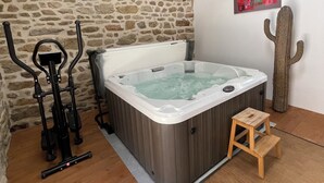 Una bañera de hidromasaje en una habitación con pared de piedra, suelo de madera y un taburete pequeño de madera.