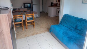 En kompakt opholdsstue med spiseplads, tekøkken og en blå sofa.