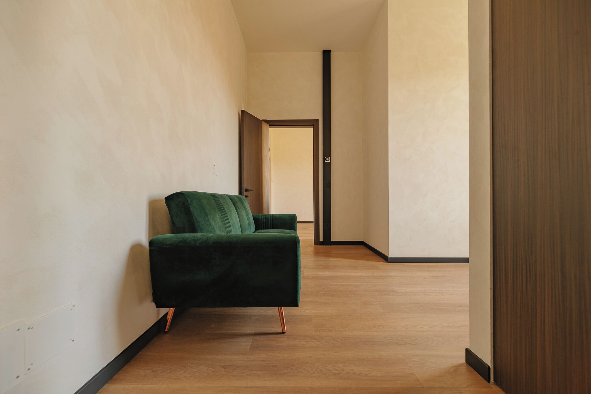 Una habitación moderna con un sofá verde, suelo de madera y una puerta que da a otra habitación.