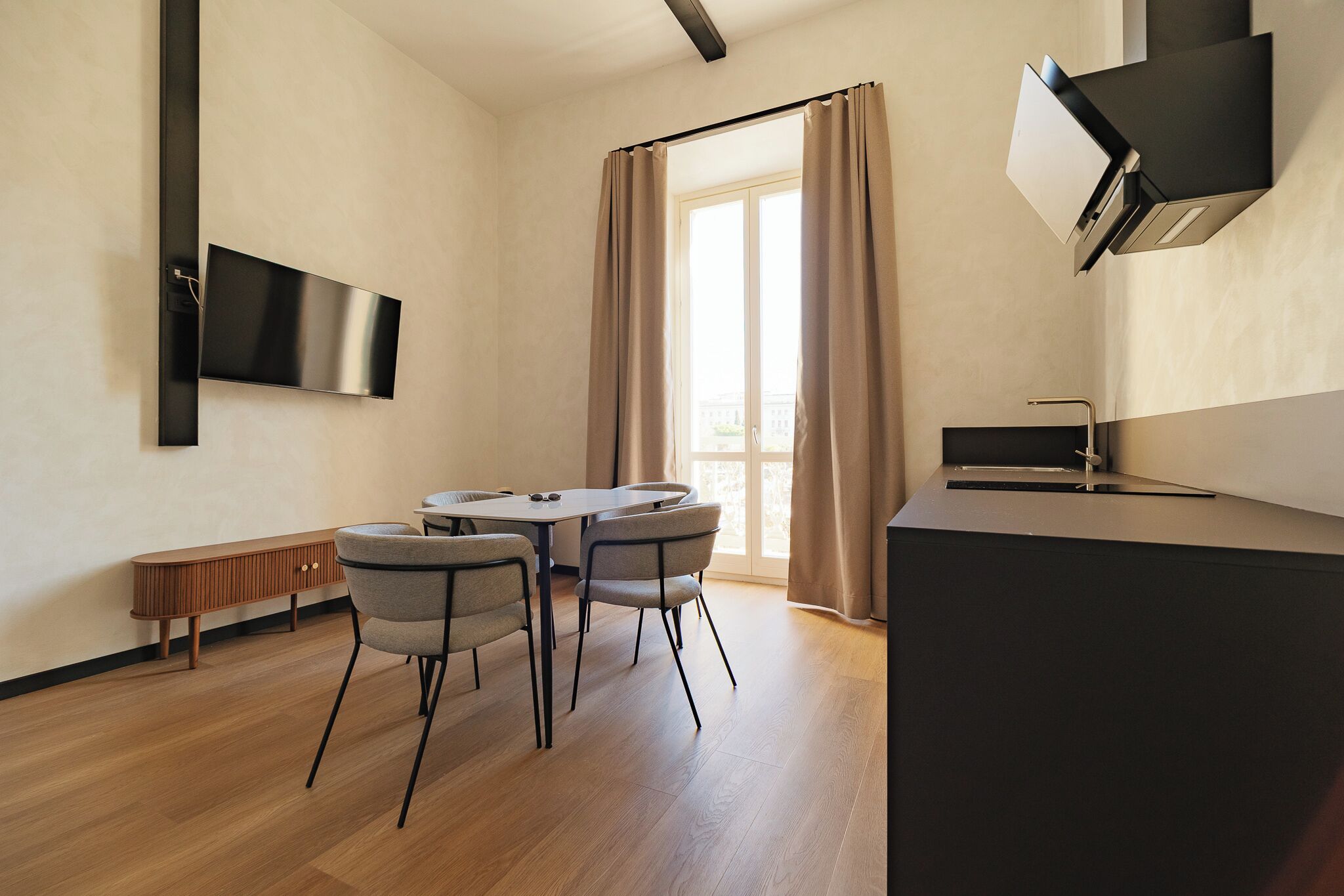 A modern kitchen with a dining area, a flat-screen TV, and a large window with curtains.