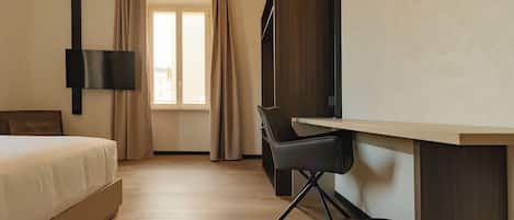 A modern hotel room with a bed, a desk, a chair, a TV, and a window with curtains.