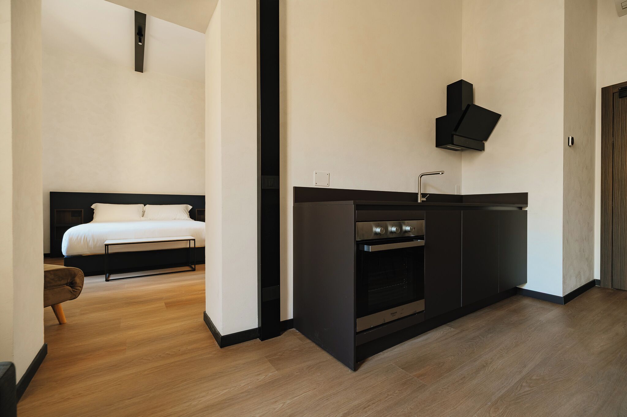 A modern hotel room with a kitchenette, a bed, and a wooden floor.