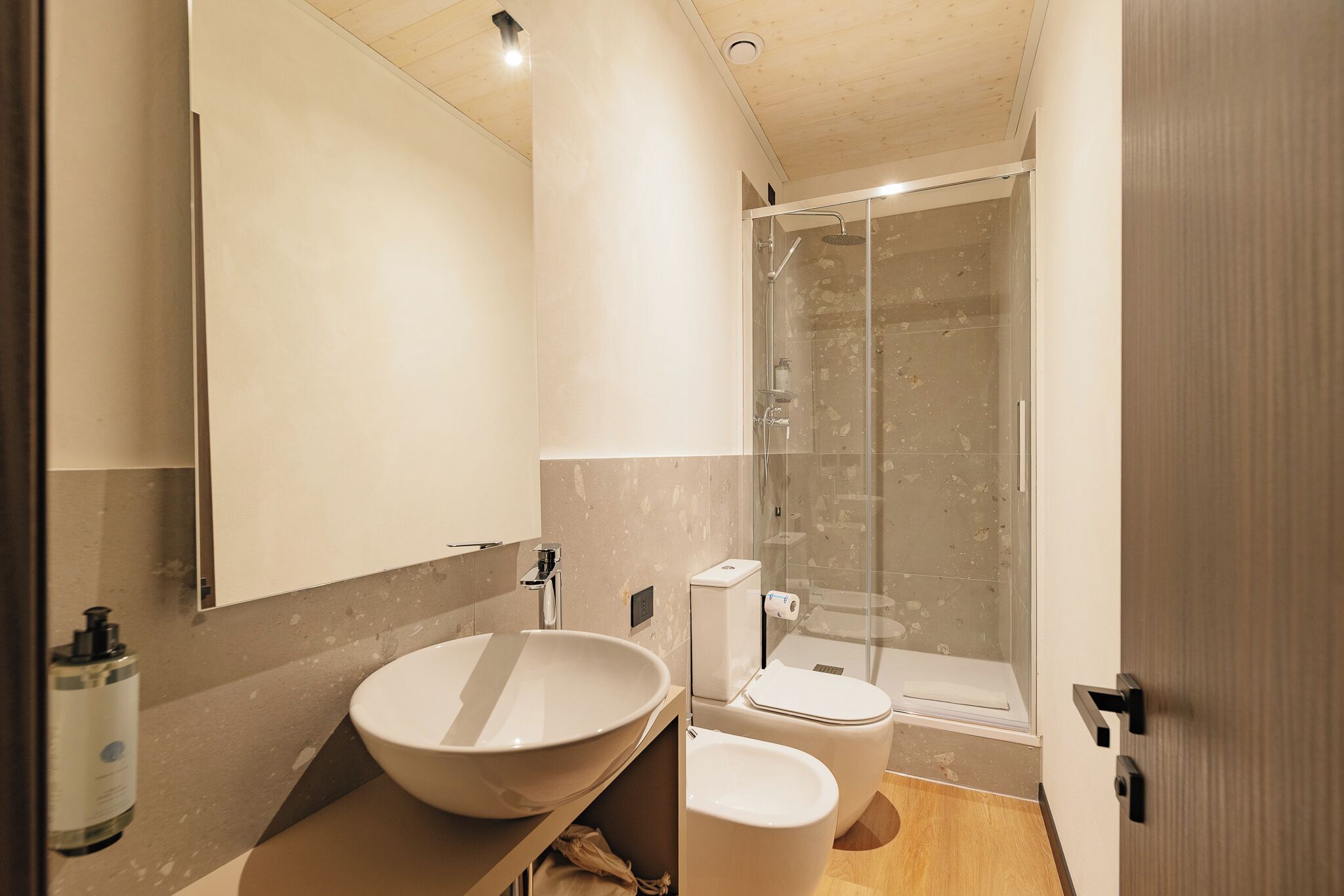 A modern bathroom with a large white sink, a toilet, and a glass-enclosed shower.
