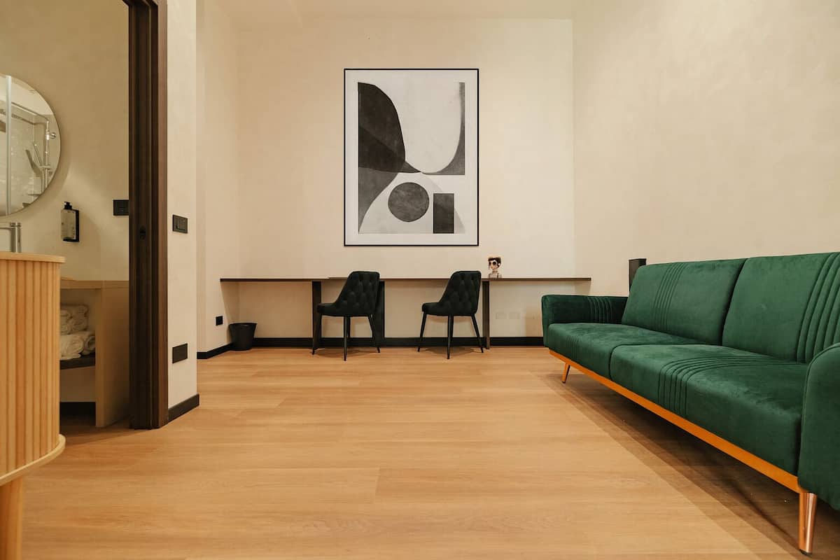 Ein modernes Wohnzimmer mit einem grünen Sofa, zwei schwarzen Sesseln und einem großen, abstrakten Gemälde an der Wand.
