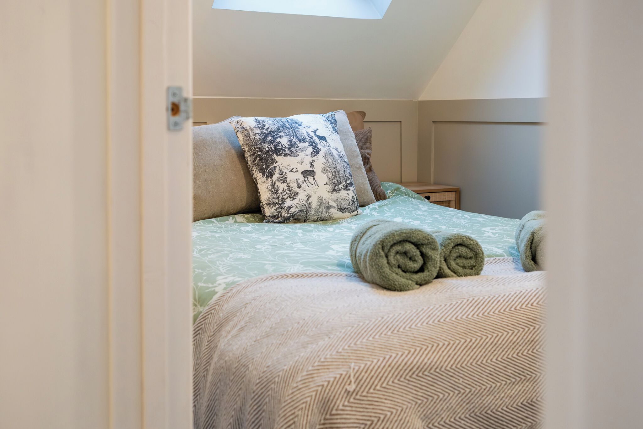 A bedroom with a bed, pillows, and rolled towels.