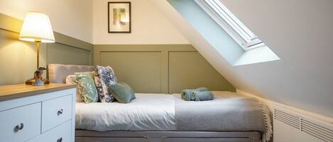 Un dormitorio con cama, mesita de noche, lámpara y un cuadro en la pared.
