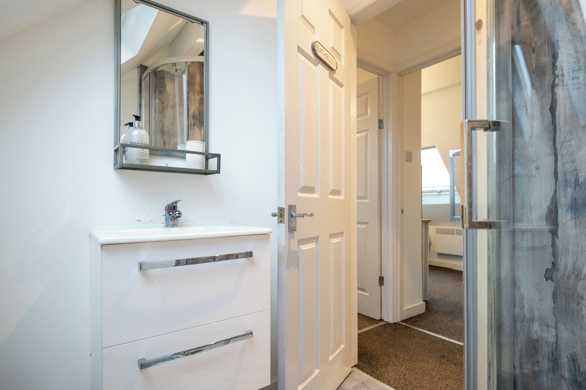 Un baño con tocador blanco, un espejo y una puerta que da a otra habitación.