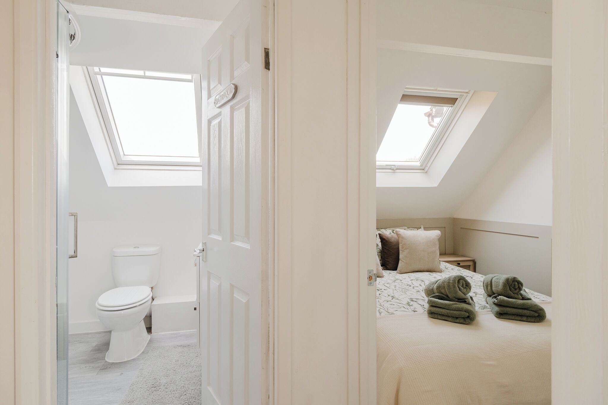 A bedroom with a skylight, a bed with rolled towels, and a nightstand.