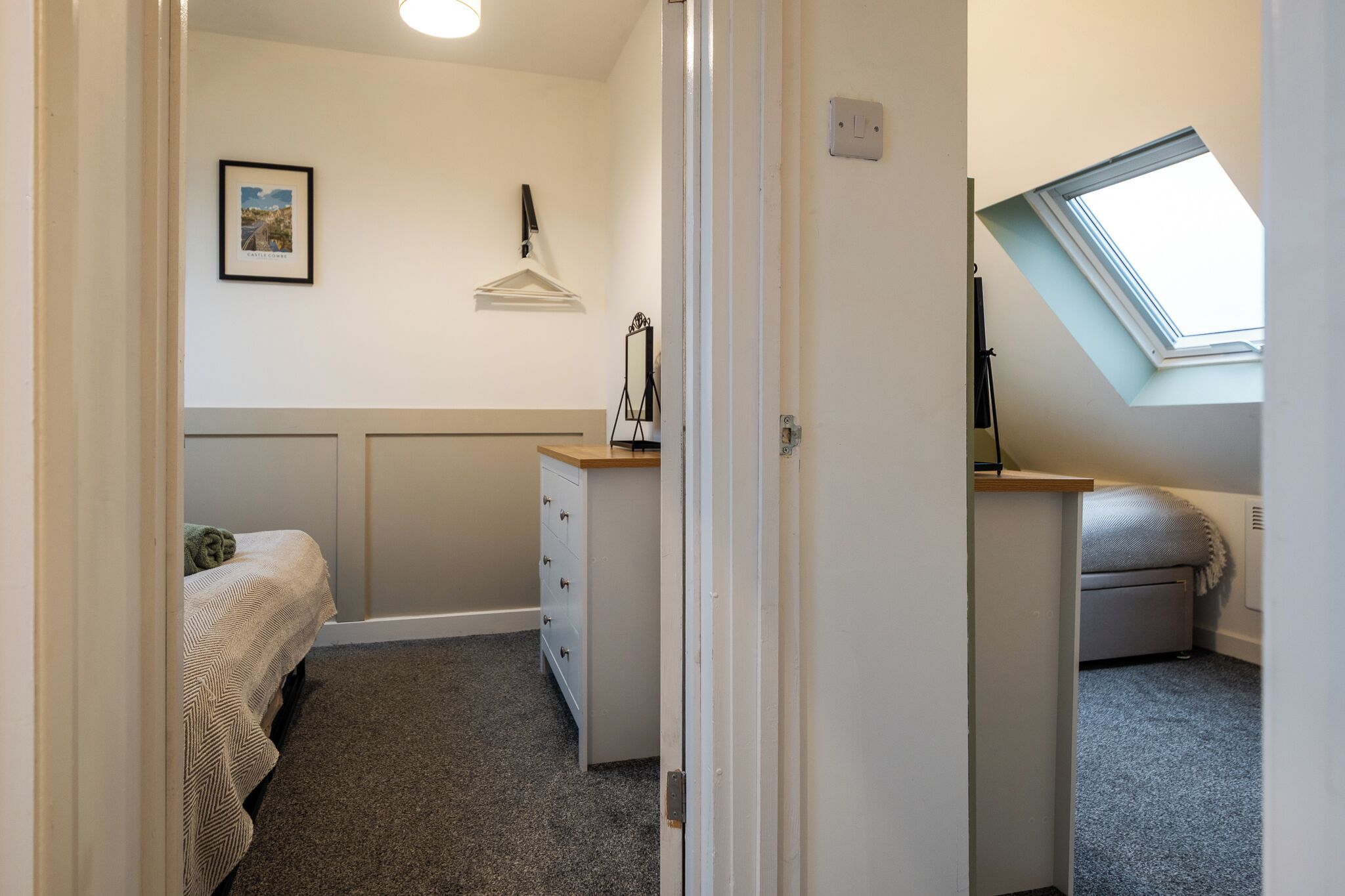 A bedroom with a bed, dresser, and a skylight.