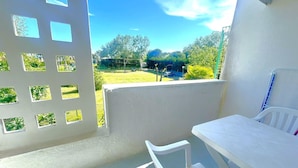 Un balcon avec une table et une chaise blanches, une vue sur un parc verdoyant et un ciel dégagé.
