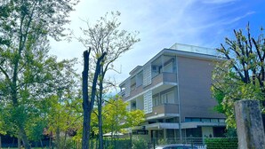 Un immeuble résidentiel à plusieurs étages, doté de balcons, entouré d’arbres et comprenant un espace de stationnement clôturé.