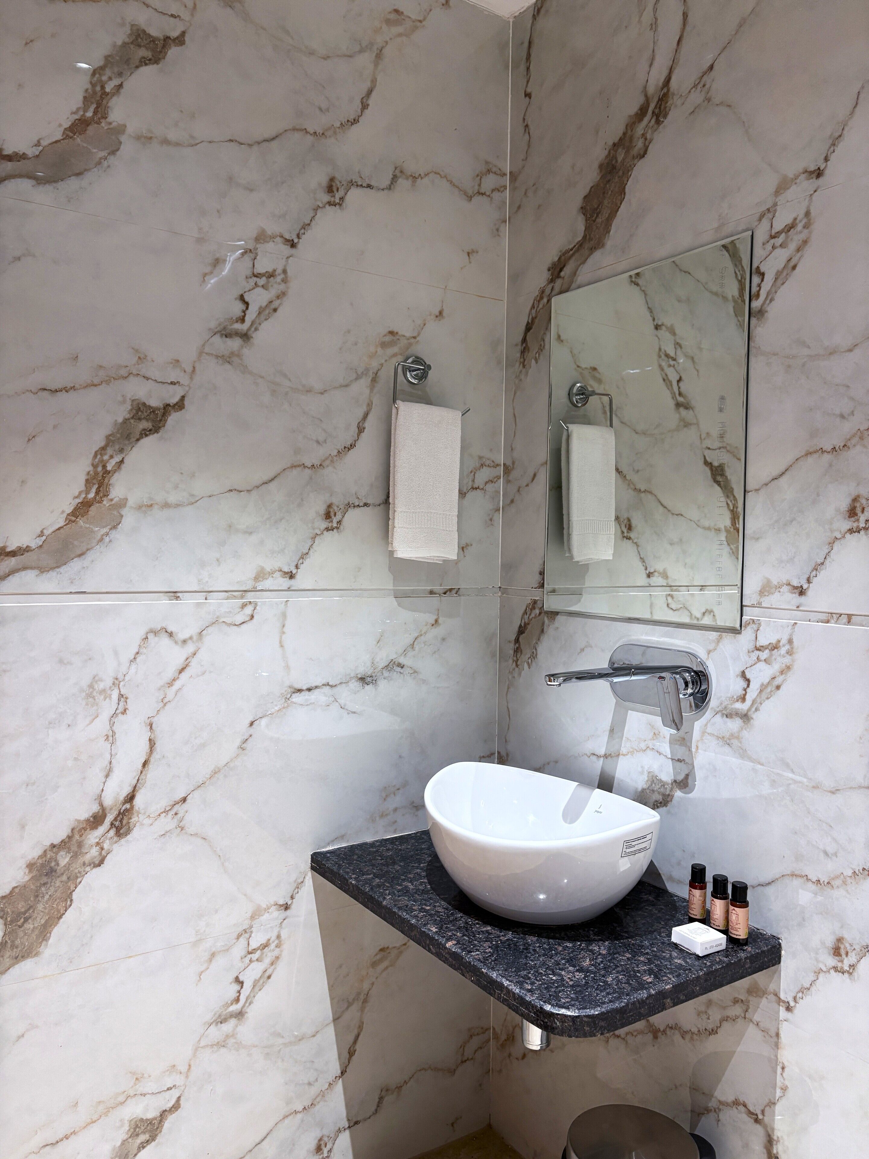 Un baño con pared de mármol, un lavamanos con espejo y un perchero para toallas.