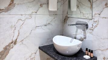 Un baño con pared de mármol, un lavamanos con espejo y un perchero para toallas.