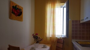 A small dining area with a table, chairs, a vase with flowers, and a window with curtains. - Apartment Desa (Bol)