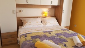 A bedroom with a bed, pillows, a nightstand, a lamp, a wooden headboard, and a yellow wall. - Apartment Desa (Bol)