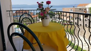 A balcony with a yellow table and chairs, a vase with flowers, and a view of the sea and buildings. - Apartment Desa (Bol)