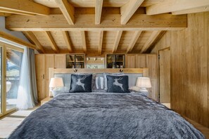Una camera da letto con soffitto in legno, un letto con coperta in pelliccia, due lampade e una finestra con tende.