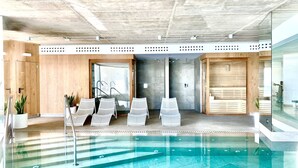 Een modern binnenzwembad met helder water, omringd door ligbedden en een sauna.