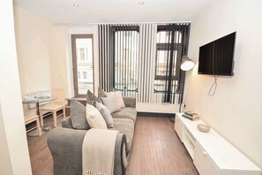 Ein modernes Wohnzimmer mit einer Couch, einem an der Wand befestigten Fernseher und einem Essbereich mit Tisch und Stühlen.