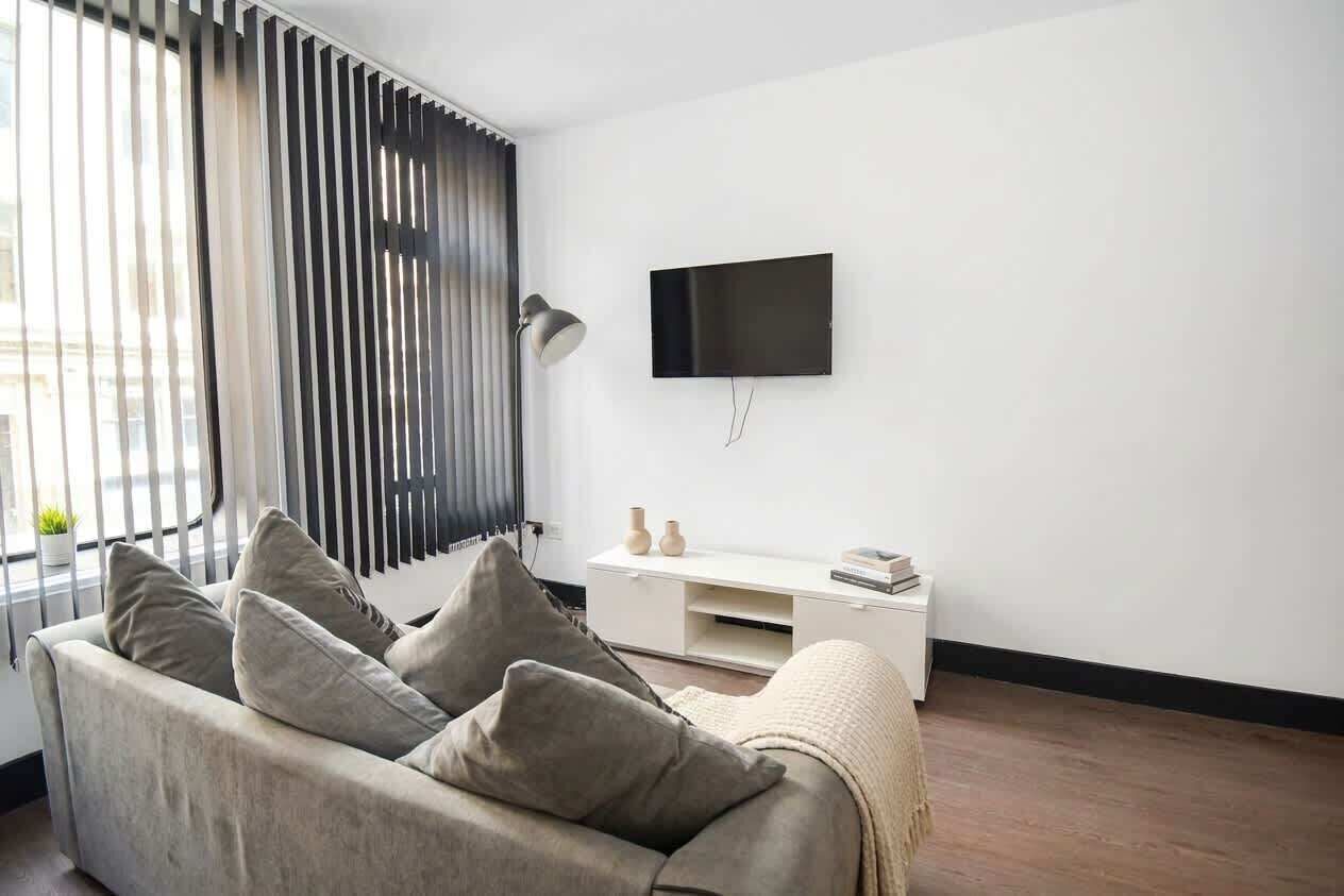 Un salon moderne comprenant un canapé, un téléviseur à écran plat fixé au mur, une console blanche et un lampadaire.