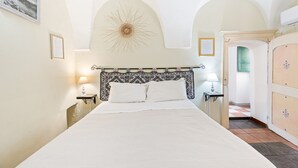 A bedroom with a bed, a wall-mounted lamp, a decorative wall piece, and a door leading to another room. - Romeo & Giulietta Rooms: double room in historic Bosa (Bosa)