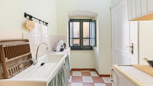 A kitchen with a sink, a kettle, a window with shutters, and a door. - Romeo & Giulietta Rooms: double room in historic Bosa (Bosa)