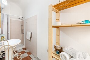 A bathroom with a shower, sink, and wooden shelves. - Romeo & Giulietta Rooms: Double Room in Historic Bosa (Bosa)
