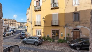 Una vista di strada con auto parcheggiate, un edificio giallo con balconi e una strada acciottolata.