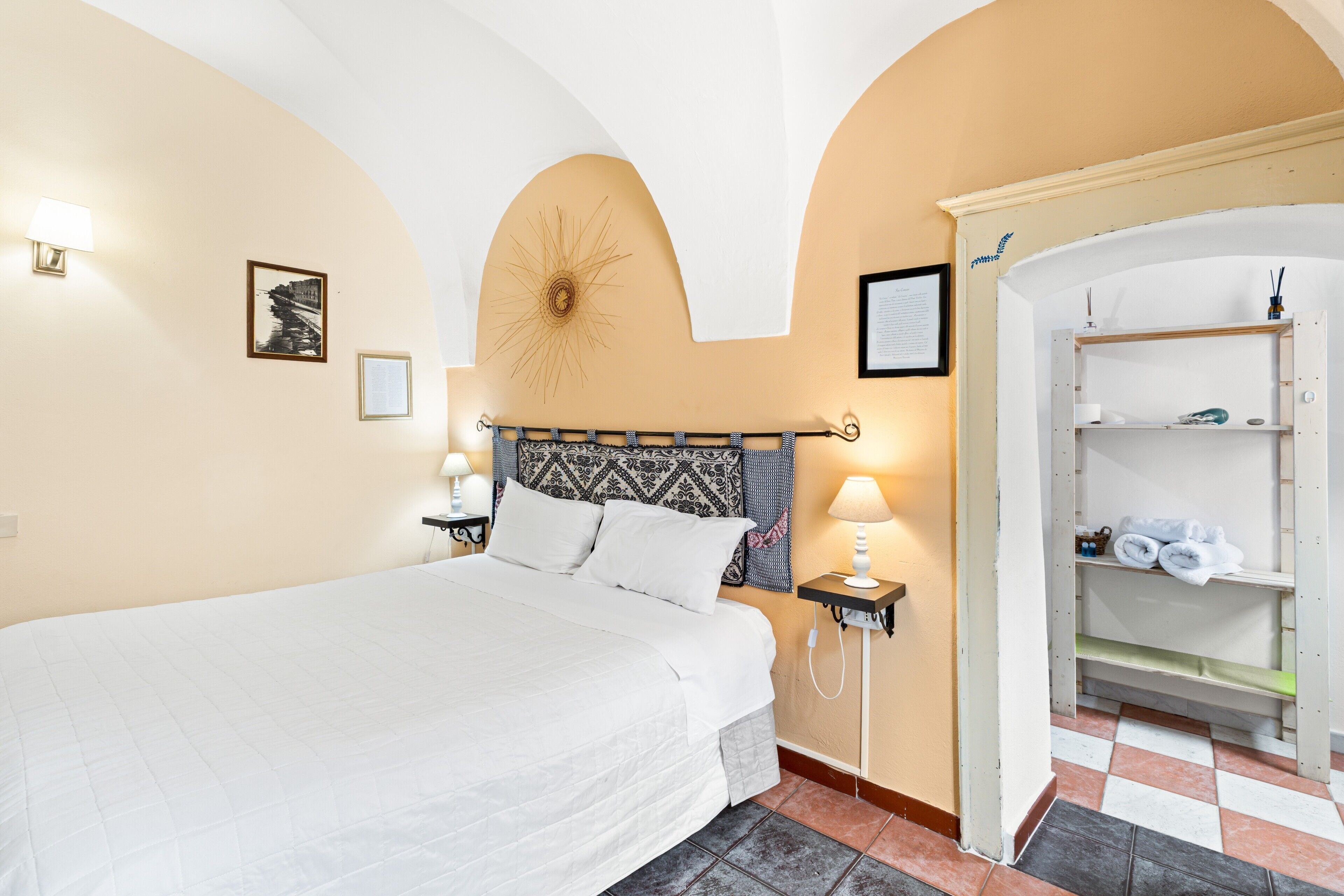 Ein Hotelzimmer mit einem Bett, einem Nachttisch mit Lampe, einem an der Wand befestigten Regal und einem Schachbrettmuster-Boden.