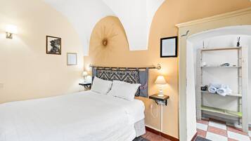 Ein Hotelzimmer mit einem Bett, einem Nachttisch mit Lampe, einem an der Wand befestigten Regal und einem Schachbrettmuster-Boden.