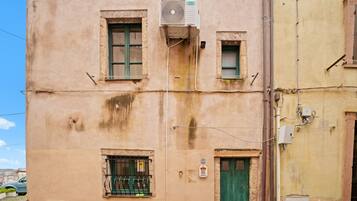 A building with a green door, a window with a metal grill, and an air conditioning unit mounted on the wall.
