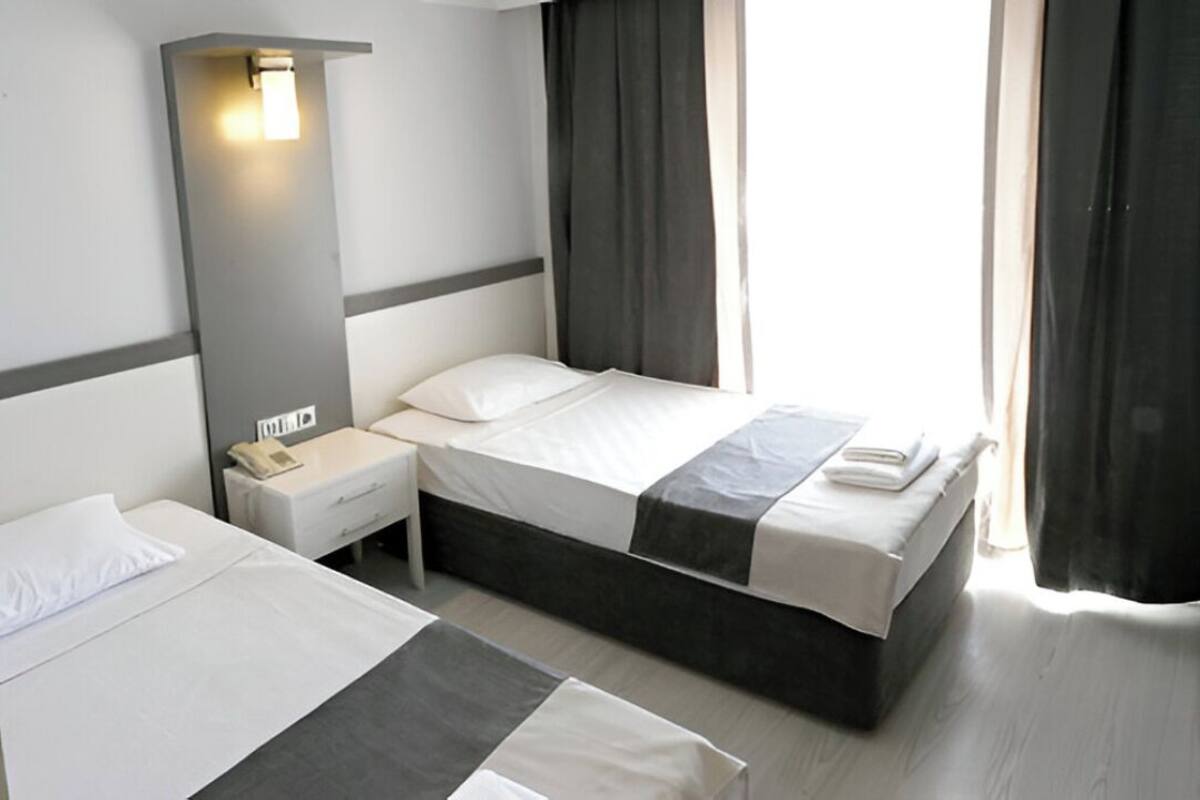 Een hotelkamer met twee bedden, een nachtkastje met telefoon, een wandlamp en een raam met gordijnen.