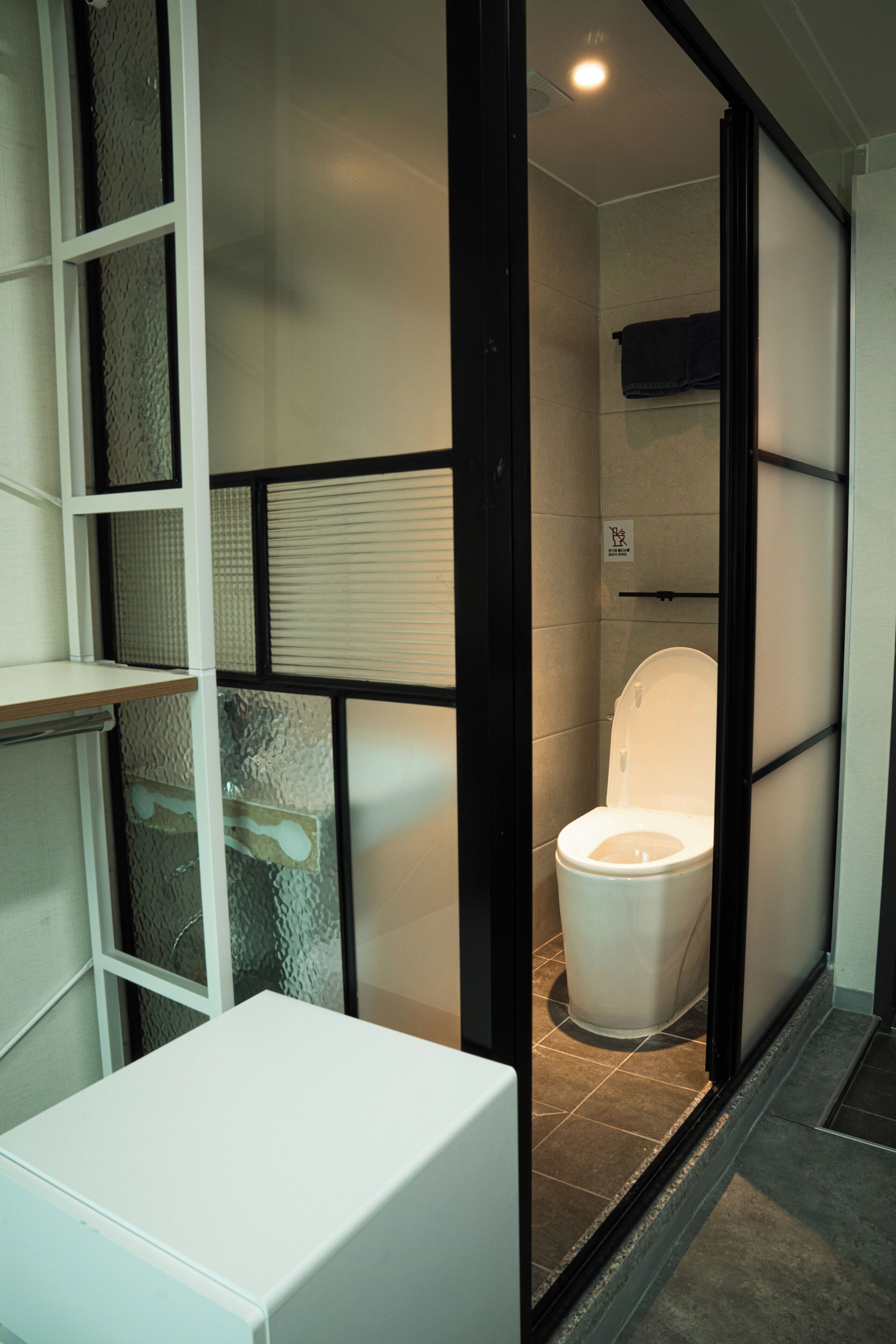 A compact bathroom with a white toilet, a small shelf, and a towel hanging on the wall.
