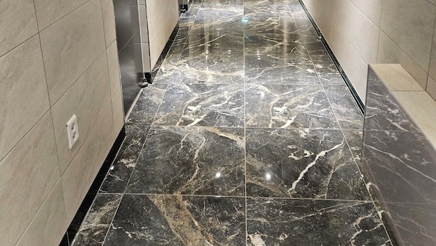A long, narrow hallway with a marble floor, tiled walls, and a series of doors on one side.