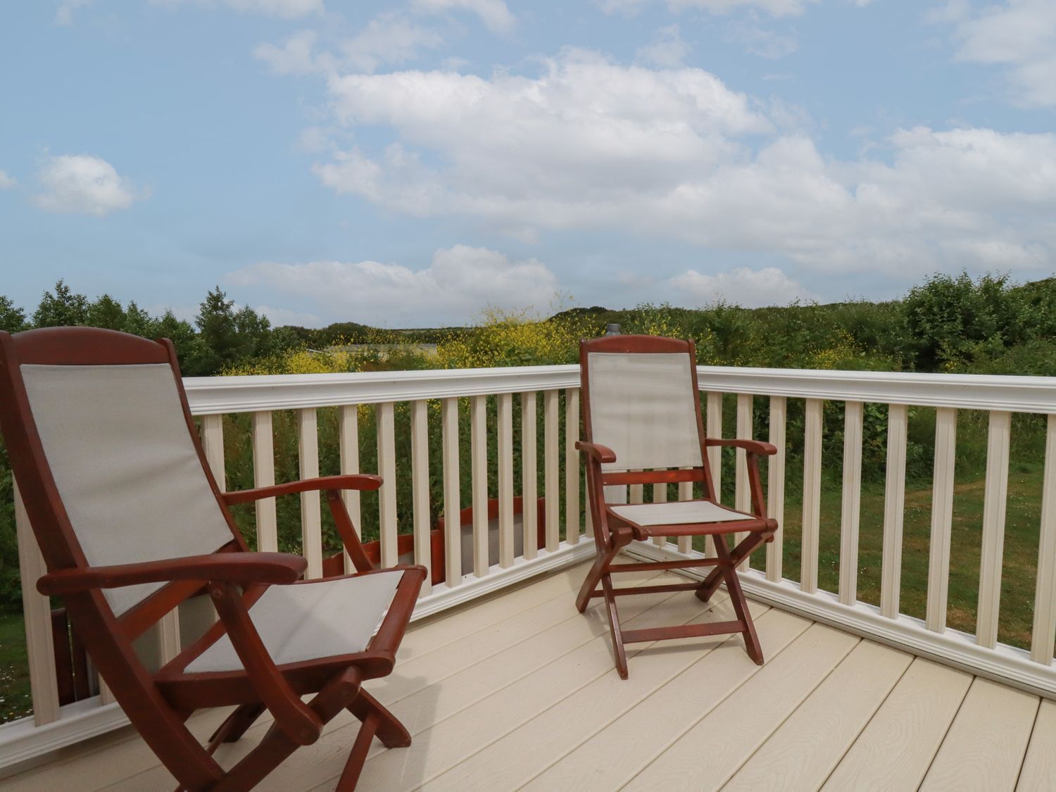 A wooden deck with two Adirondack chairs facing a white railing.