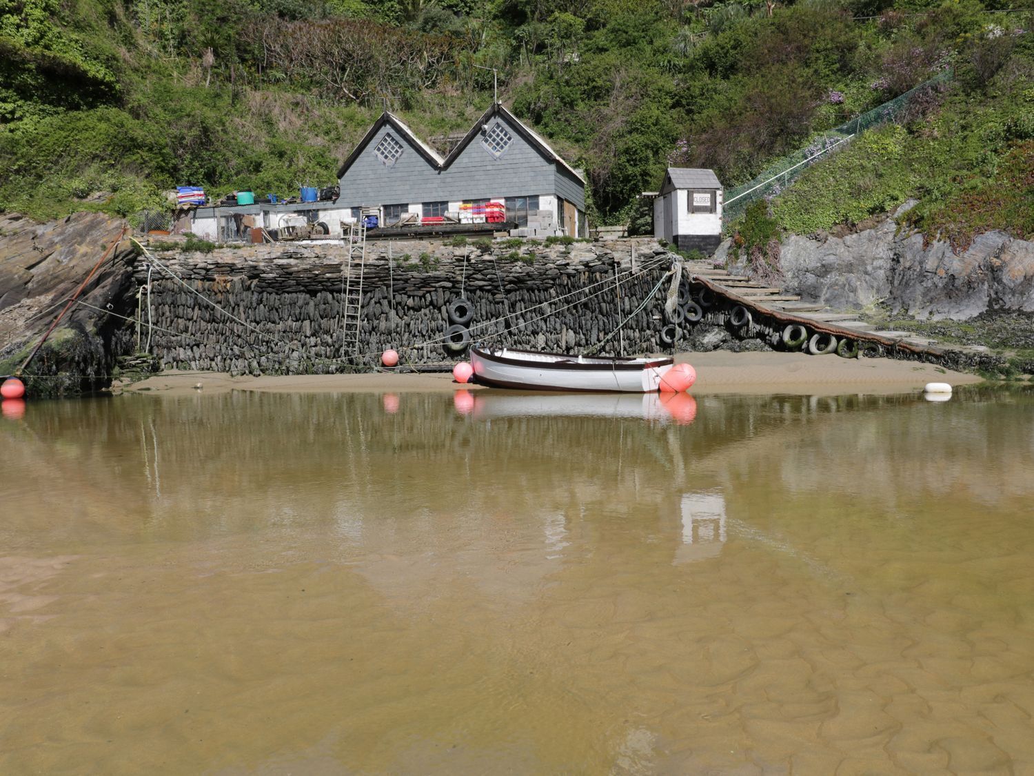 A coastal house with a stone wall and a small boat docked in the water.