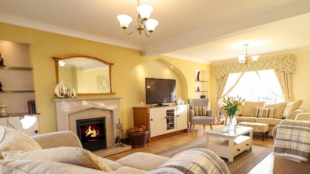 A living room with a fireplace, sofa, television, and a dining area with a table and chairs. - Llwyn Derw (Talybont)