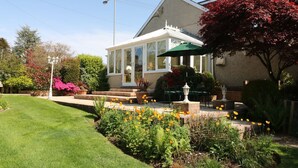 A house with a conservatory, surrounded by a well-maintained garden with various plants and flowers. - Llwyn Derw (Talybont)