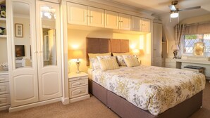 A bedroom with a large bed, a wardrobe, a vanity, and a ceiling fan. - Llwyn Derw (Talybont)