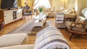 A living room with a sofa, armchairs, a coffee table, a TV, and a bookshelf. - Llwyn Derw (Talybont)